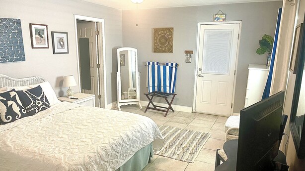 A bedroom with a bed, a dresser, a mirror, a television, and a door. - One Bedroom Apartment, One block from the beach BTR #2197 (Indian Rocks Beach)