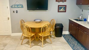 A dining area with a round table, four wooden chairs, a black trash can, a kitchen sink, and a framed picture on the wall. - One Bedroom Apartment, One block from the beach BTR #2197 (Indian Rocks Beach)