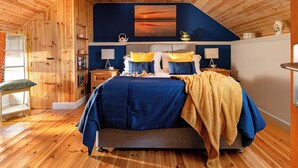 A bedroom with a wooden ceiling, a bed with blue bedding, two bedside tables with lamps, a nightstand, and a wall-mounted shelf. - Coach House - UK38039 (Honeyborough)