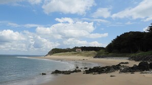 A beach with a rocky shoreline, a sandy beach, and a house on a hill in the background. - Coach House - UK38039 (Honeyborough)