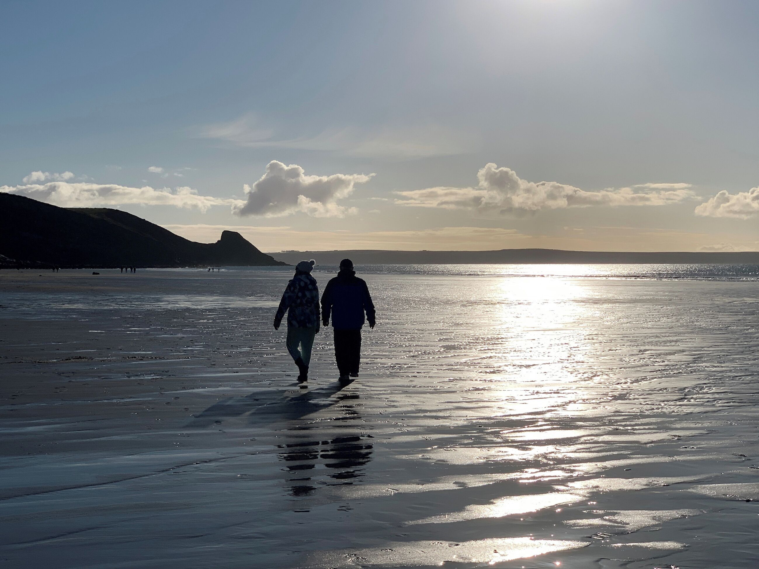 Deux personnes se promènent sur une plage, avec une montagne en arrière-plan.