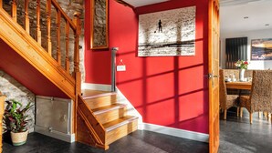 A staircase with wooden railings leading to a room with red walls, a dining area with wicker furniture, and a stone wall. - Coach House - UK38039 (Honeyborough)