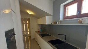 Een moderne keuken met witte kasten, een inbouwoven, een dubbele spoelbak en een raam boven de spoelbak.