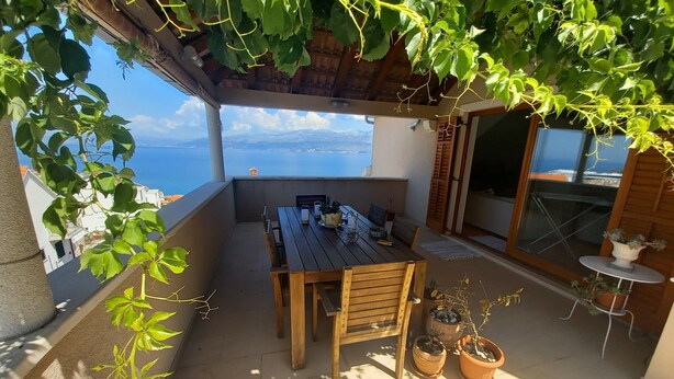Een houten tafel met stoelen op een balkon, met plantenpotten, met uitzicht op een schilderachtig panorama.