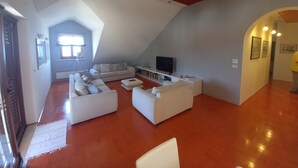 Een ruime woonkamer met een hoge plafond, een groot raam en een televisie.
