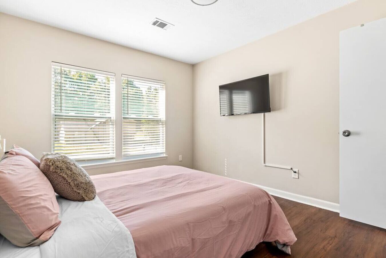 Een slaapkamer met een bed, een aan de muur bevestigde televisie en een deur.