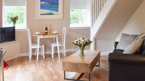 A dining area with a wooden table, white chairs, a painting above, and a staircase to the right.