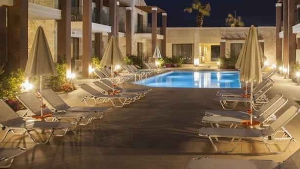 A pool area with lounge chairs and umbrellas, surrounded by buildings with a modern architectural style. - Althea Village Hotel (Chania)