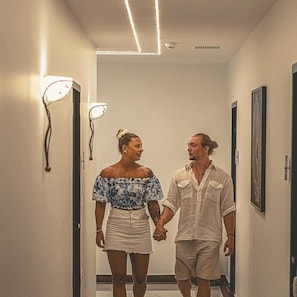 A hallway with a modern design, featuring wall-mounted lighting and framed artwork. - Althea Village Hotel (Chania)