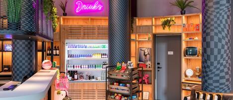 A modern interior with a neon sign reading "Food & Drinks," a wooden counter with a variety of beverages, and a cozy seating area with a checkered cushion.