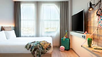 A hotel room with a bed, a television, a suitcase, and a desk with a lamp.