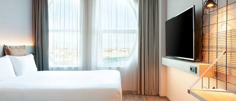 Une chambre d’hôtel moderne avec un grand lit, un téléviseur à écran plat fixé au mur et une fenêtre avec des rideaux.