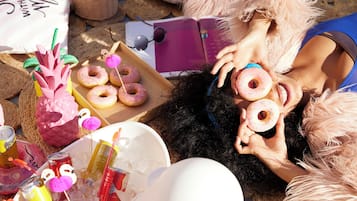 Uma pessoa deitada no chão com uma caixa de donuts, um livro e uma garrafa de bebida.