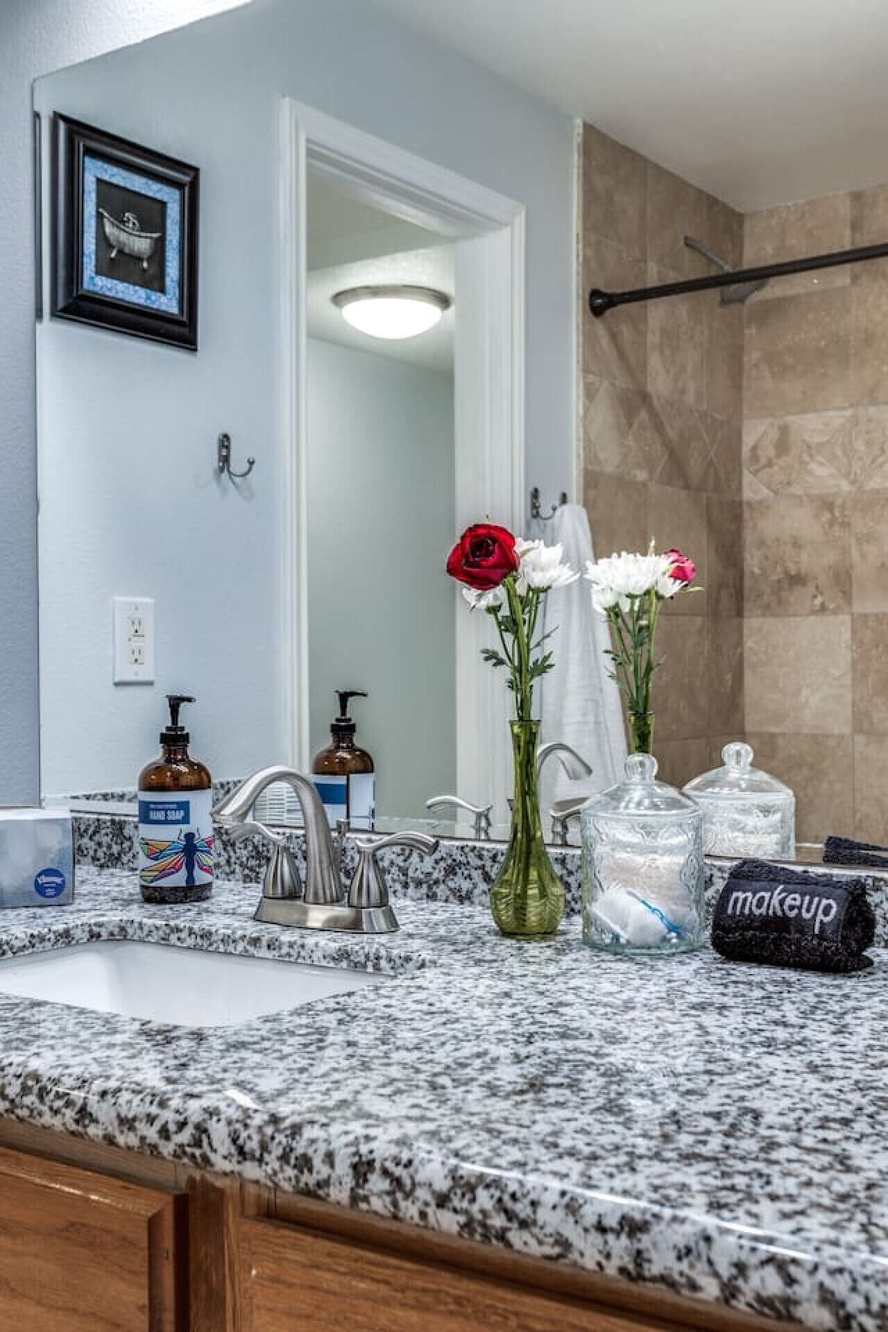 Une salle de bain dotée d’un comptoir en granit, d’un lavabo, d’un miroir, d’un porte-serviettes et d’un espace douche.