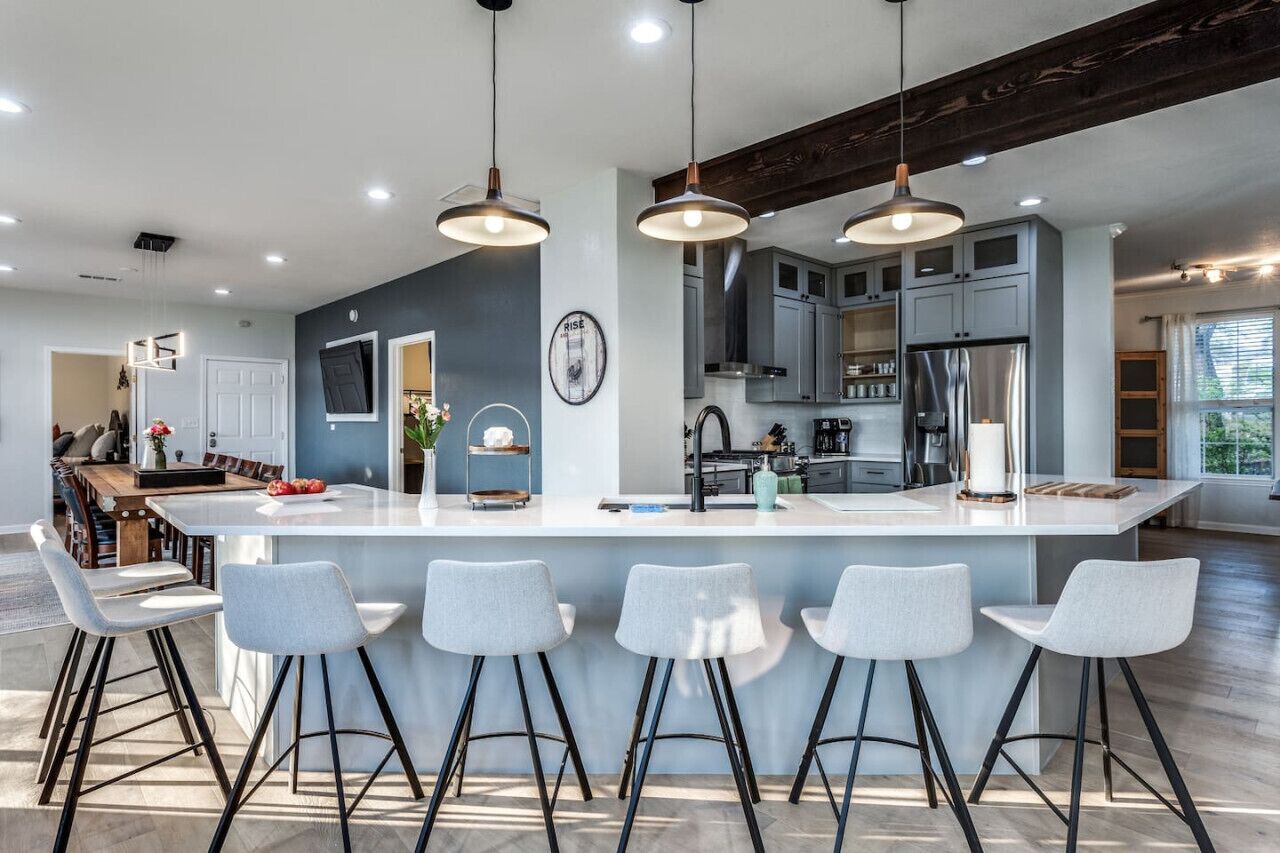 Une cuisine moderne dotée d’un îlot central, de tabourets de bar, de luminaires suspendus et offrant une vue sur l’espace repas.