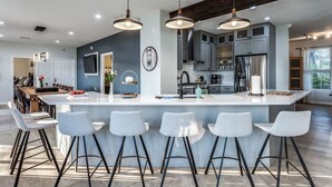 Cozinha moderna com ilha central, banquetas, iluminação pendente e vista para a sala de jantar.