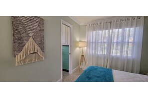 Relax in a serene space with a comfortable bed, wall-mounted artwork, and a window with sheer curtains.