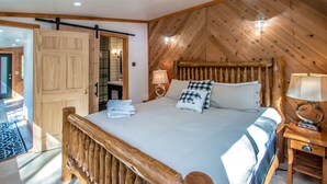 Un dormitorio con estructura de madera, una cama, lámparas de noche y cabecero de madera.