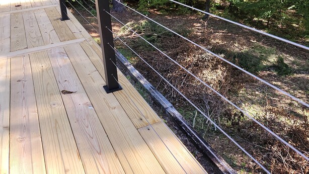 Una terraza de madera con barandas de metal, rodeada de un bosque frondoso.