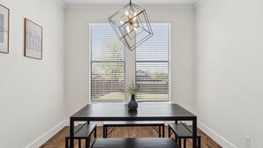 Un comedor con una mesa, bancos, un florero con plantas y una lámpara colgante de diseño geométrico.