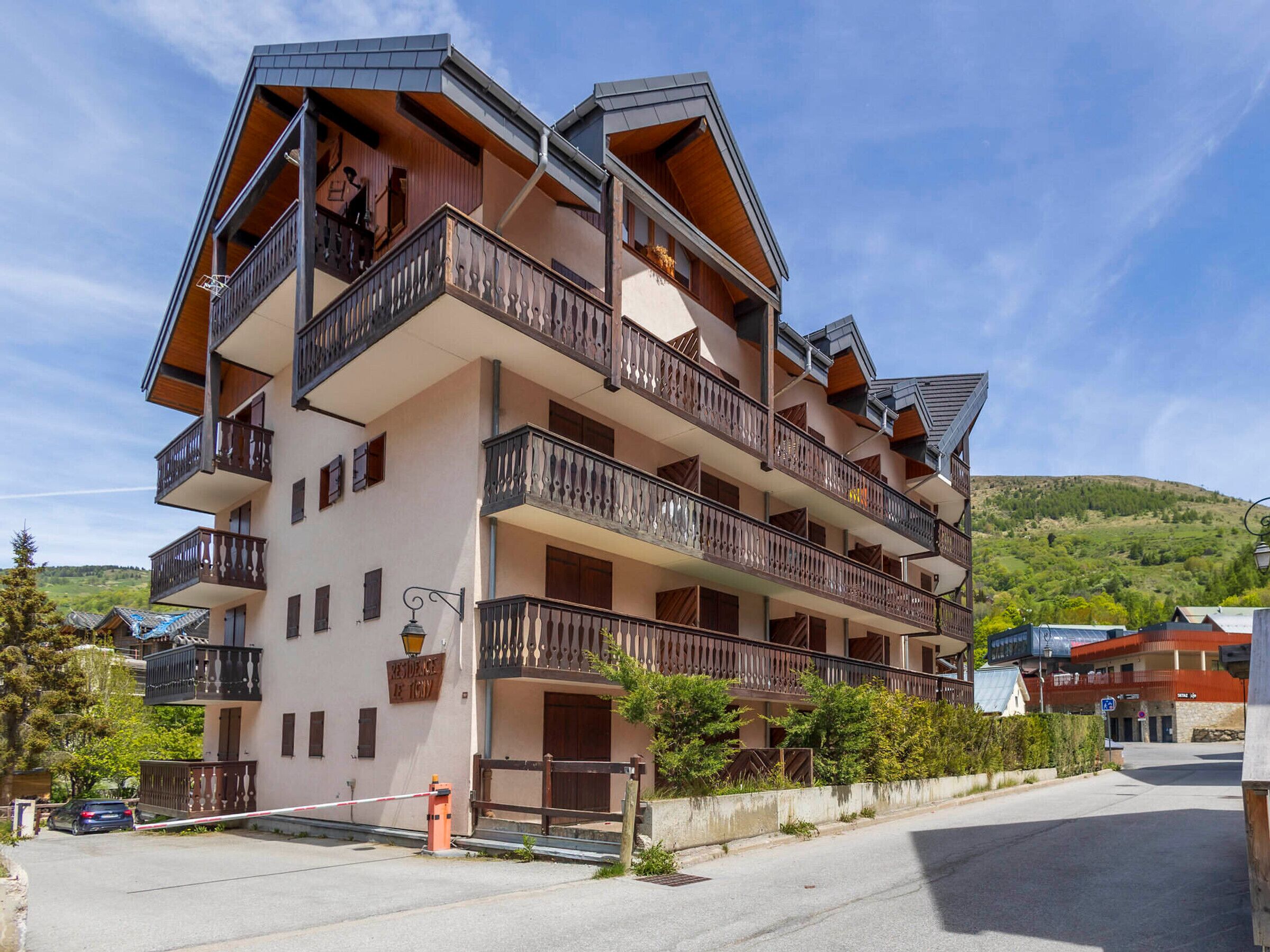 A multi-story hotel with balconies, a parking area, and a mountainous backdrop.