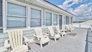 Una terraza techada con sillas Adirondack blancas y una hilera de ventanas.