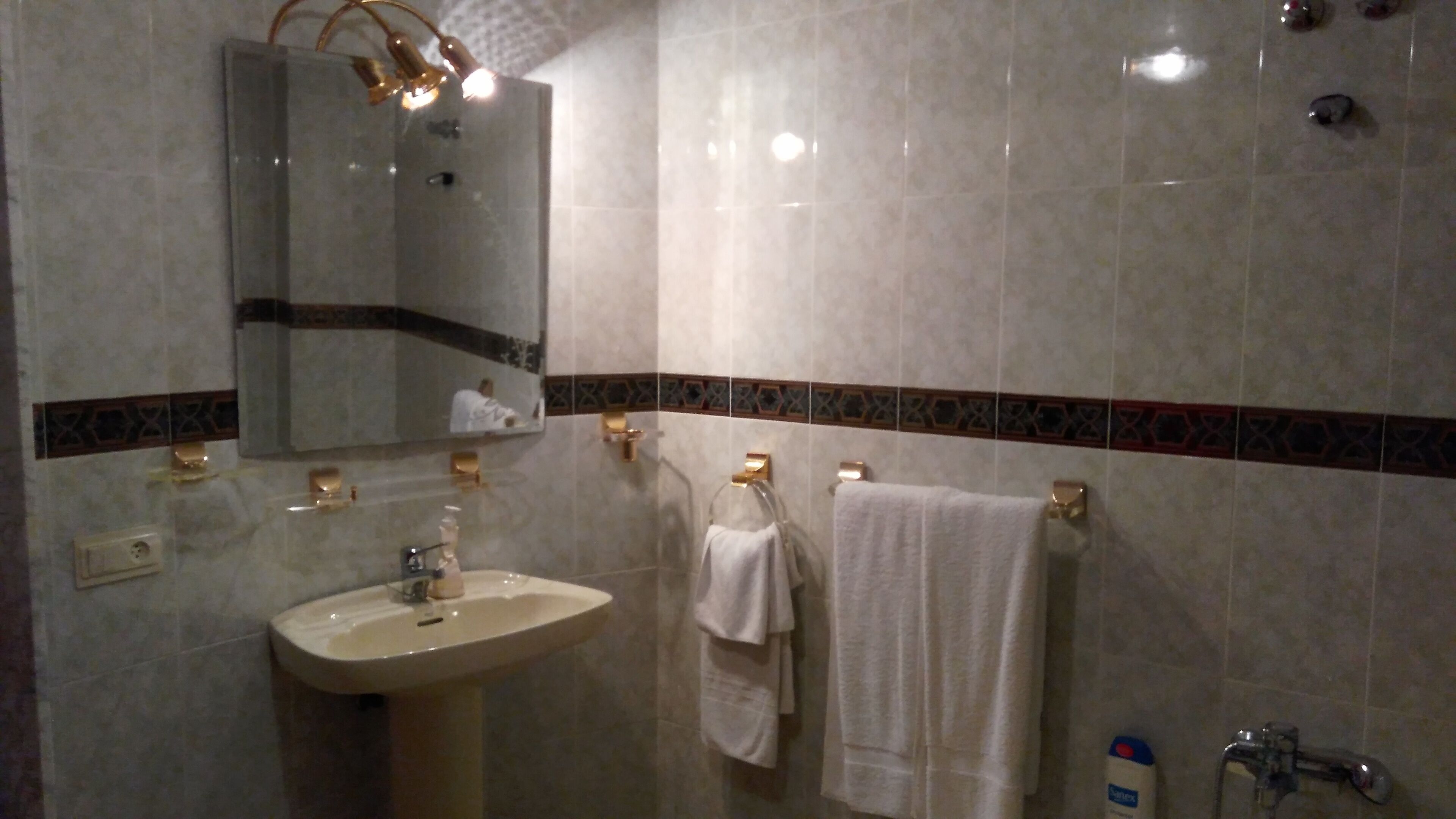 Un baño con lavamanos, espejo, toallero y ducha.