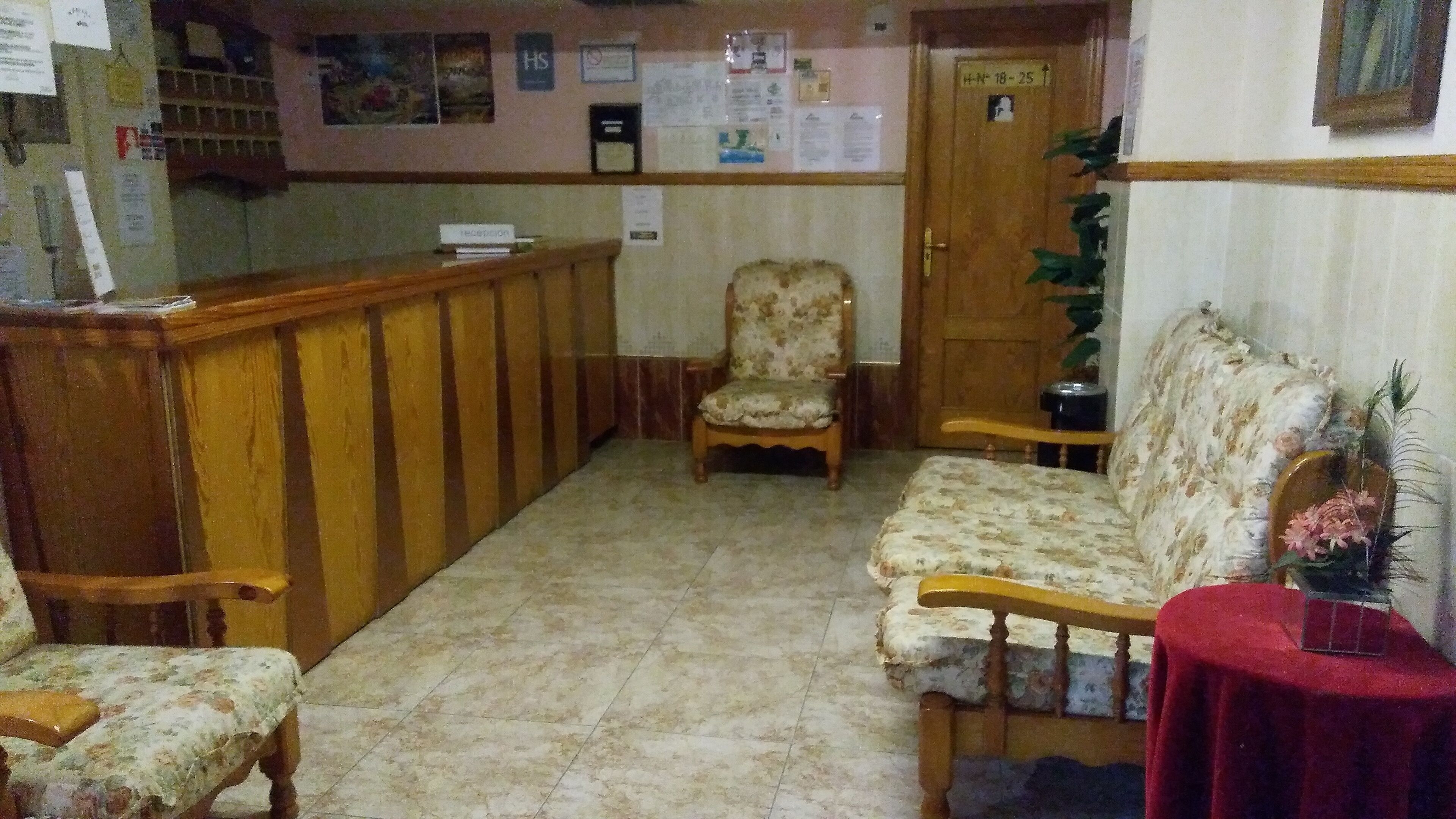 Un área de recepción con un mostrador de madera, un sofá estampado con motivos florales y una silla.