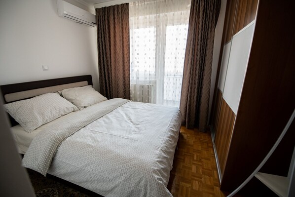 A neatly made bed with a patterned bedspread, a headboard, and a window with curtains.