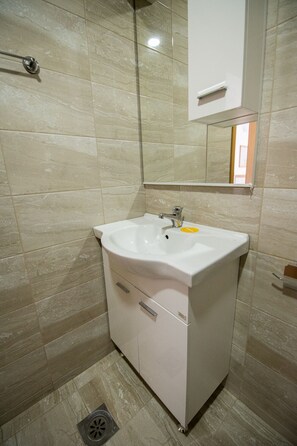 Un baño con un lavamanos blanco, un espejo y una zona de ducha.