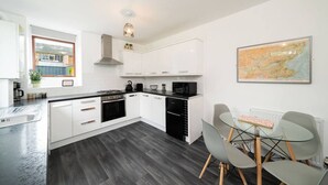 A modern kitchen with white cabinets, a black stove, and a dining area with a glass table and chairs. - The Palm - Eclectic Bliss (Broughty Ferry, Dundee)