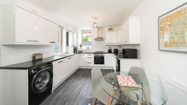 A modern kitchen with white cabinets, a washing machine, a glass table, and a map on the wall. - The Palm - Eclectic Bliss (Broughty Ferry, Dundee)