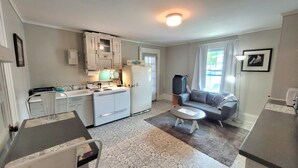A compact kitchen with a refrigerator, stove, and sink. There is a dining table with chairs and a sofa in the living area. - Vintage One Bedroom with Living/Kitchen (Mount Airy)