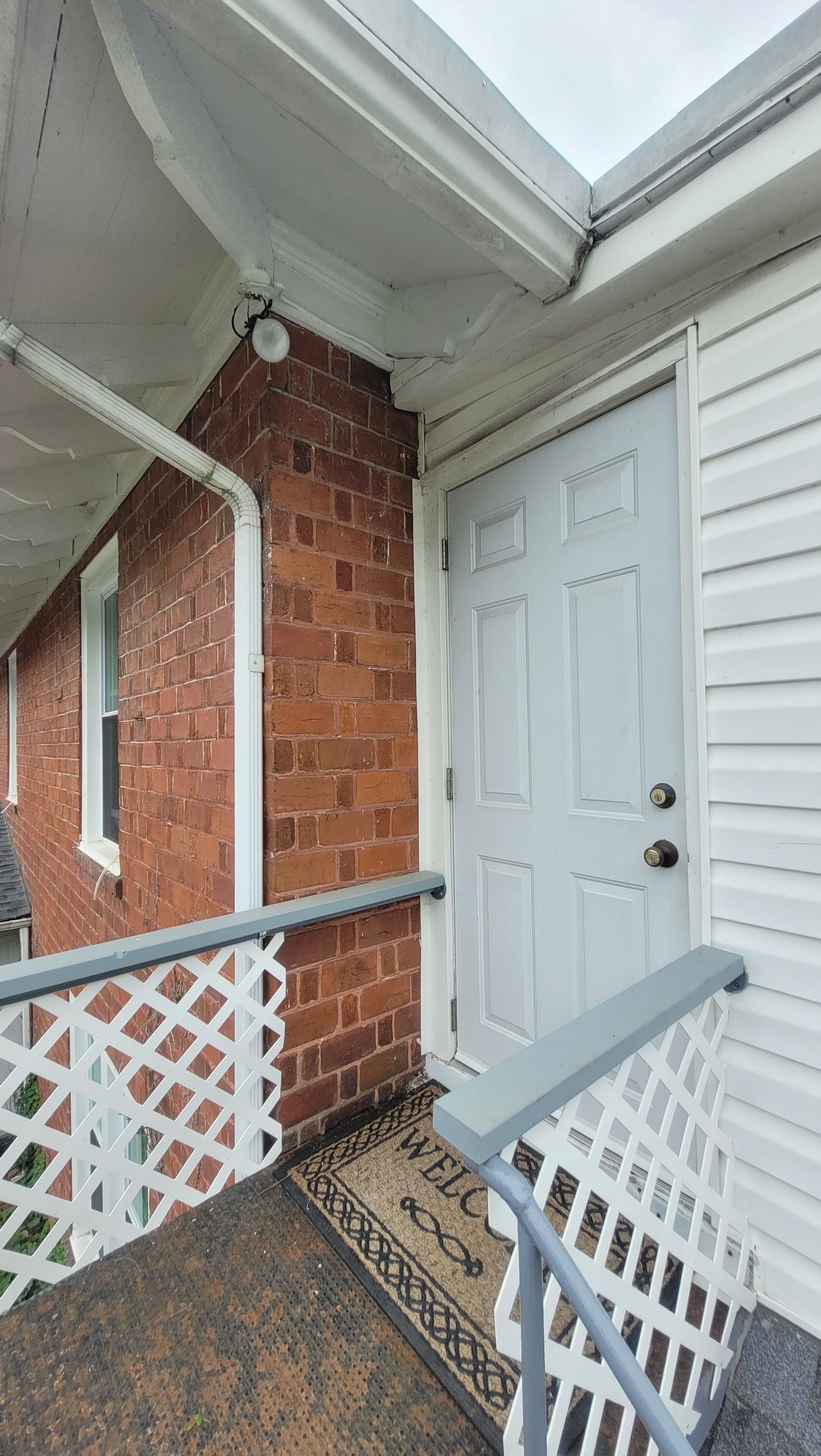 A residential entrance with a white door, a brick wall, and a white railing.