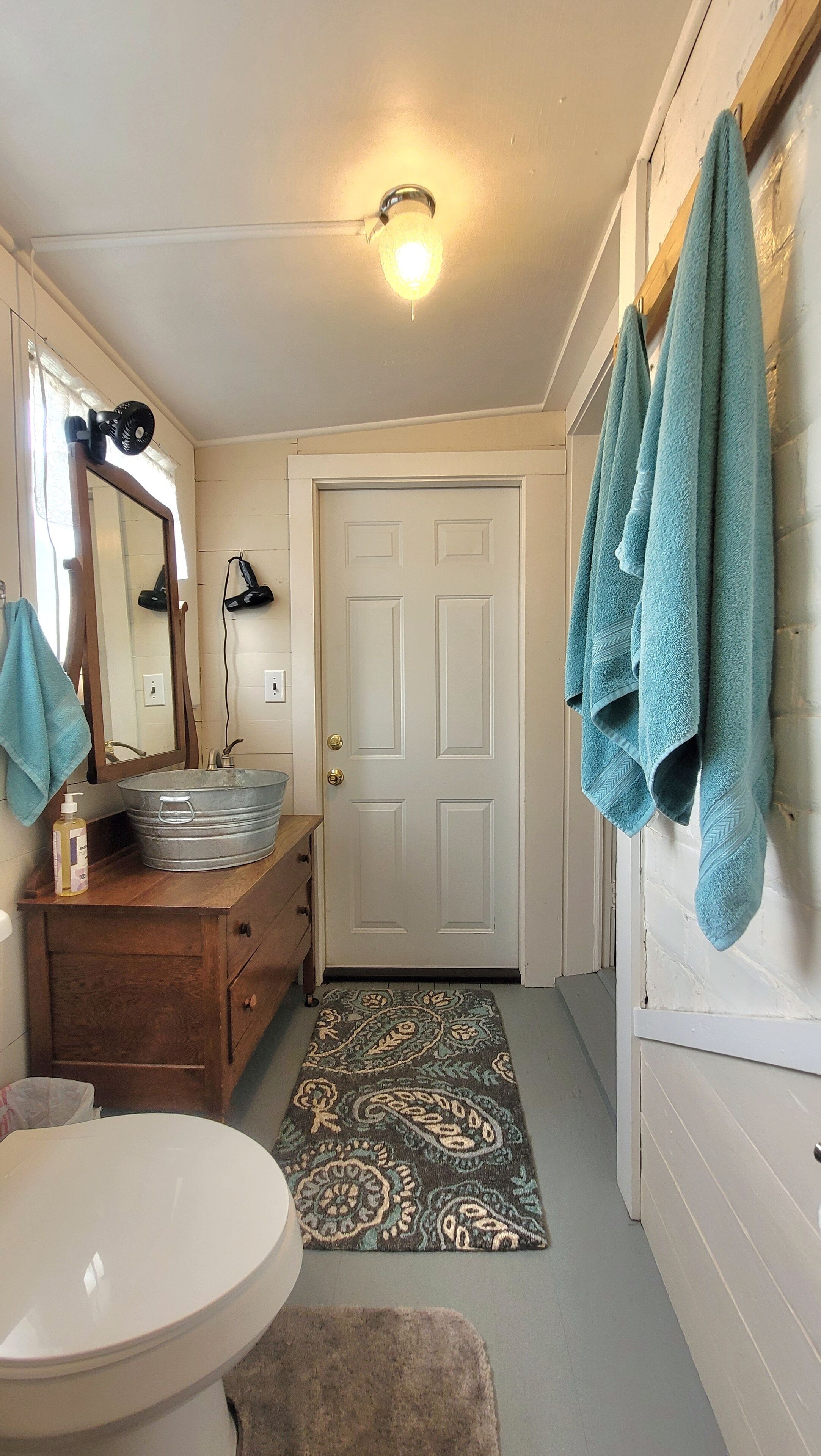 A bathroom with a white sink, a mirror, a wooden vanity, a blue towel rack, and a patterned rug.