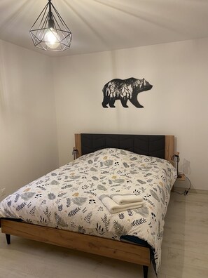A bedroom with a bed, a wall-mounted light fixture, and a bear-themed wall decal.