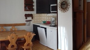 A compact kitchen with a wooden dining table and chairs, a white dishwasher, and a microwave. - 2-room apt, 4 pers, south-facing with balcony in Valloire (Valloire)