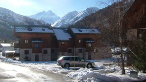 A two-story building with a sloped roof, likely a hotel or guesthouse, situated in a mountainous area with snow-covered ground and a car parked in front. - 2-room apt, 4 pers, south-facing with balcony in Valloire (Valloire)