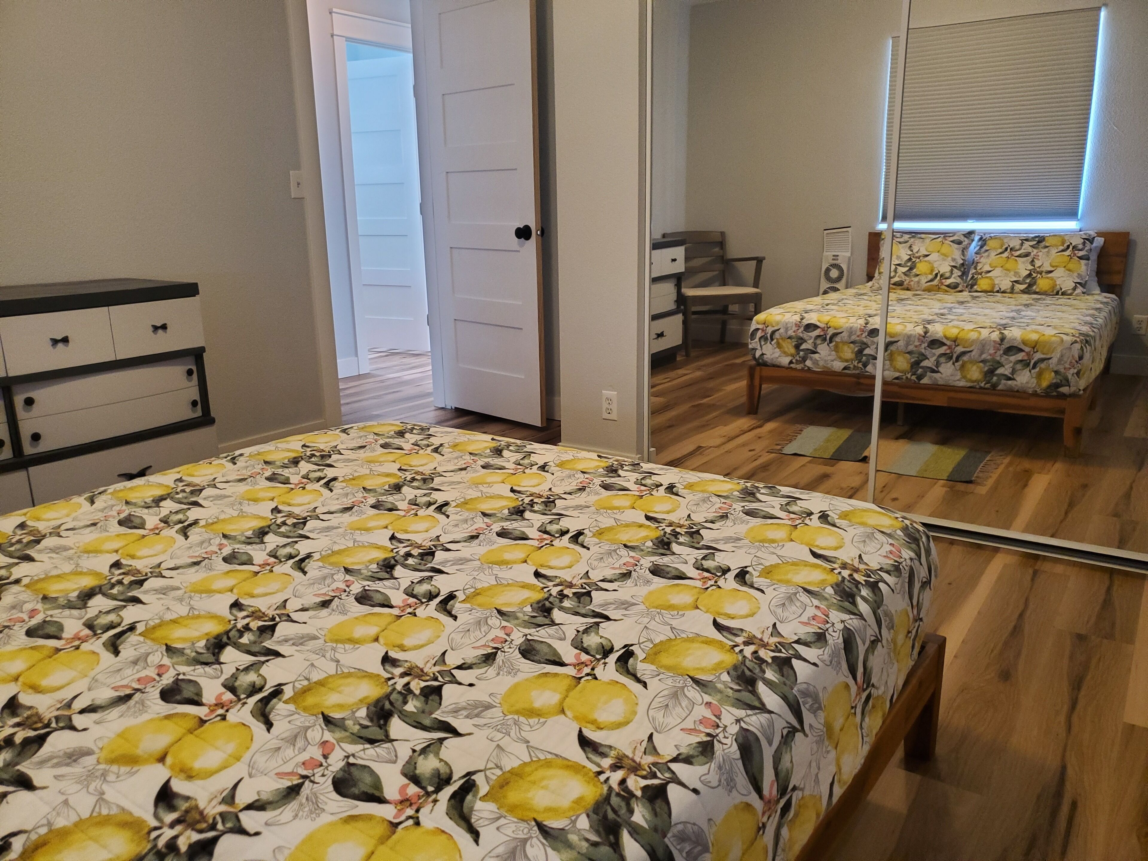 A bedroom with a bed, a dresser, a mirror, and a door leading to another room.