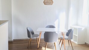 Zona pranzo moderna con tavolo bianco e quattro sedie grigie, lampada a sospensione in fibra intrecciata e pavimento in legno.