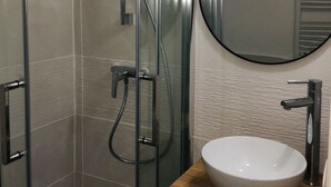 Un bagno moderno con doccia vetrata, uno specchio rotondo e un mobile contenitore in legno con lavabo bianco.
