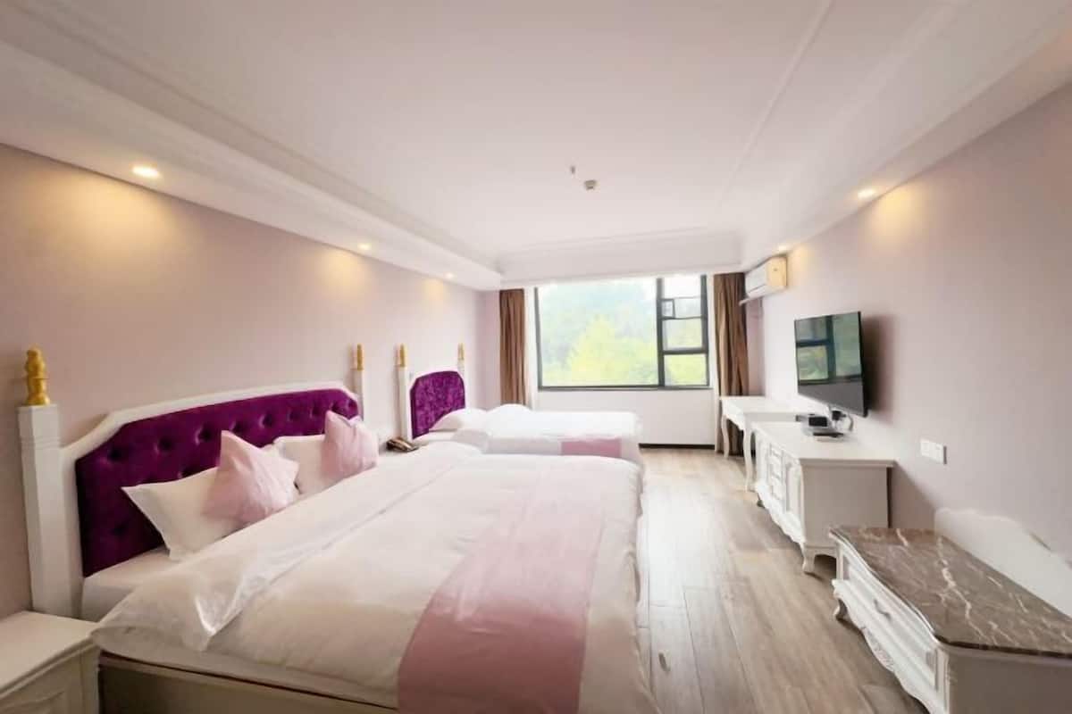 A hotel room with two beds, a TV, a desk, and a window with a view of greenery.