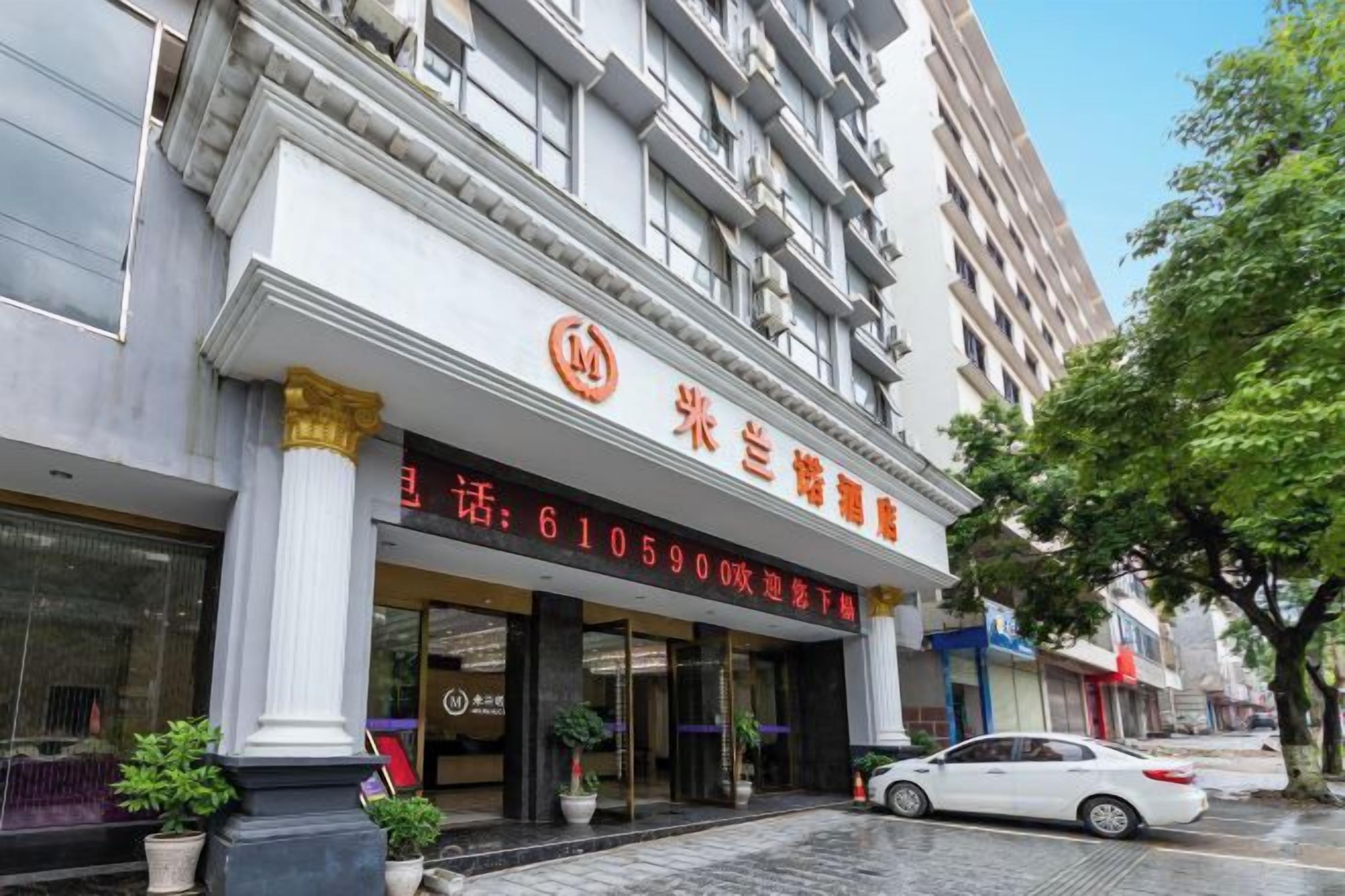 L’entrée d’un hôtel, avec une enseigne, des colonnes et une voiture garée.