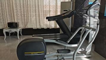 A stationary exercise bike with a digital display, a small table with a radio, and a window with curtains.