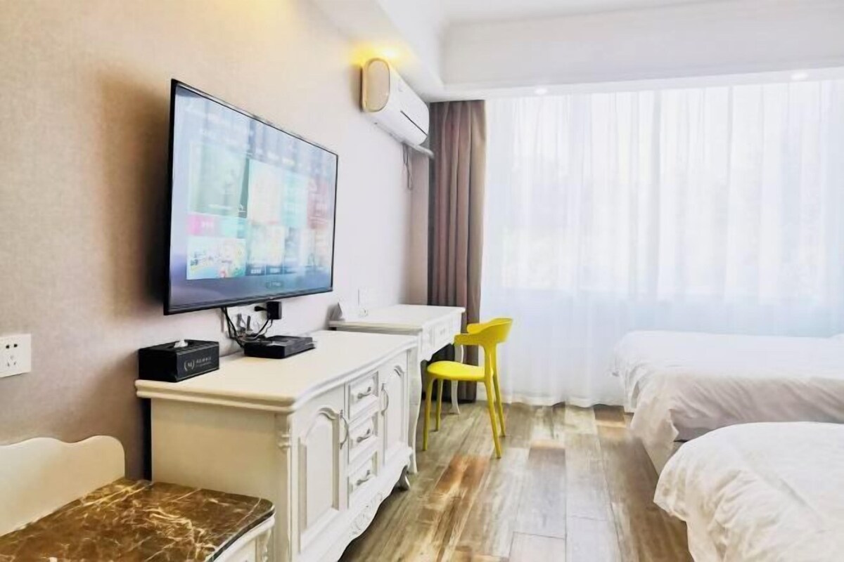 A hotel room with a flat-screen TV mounted on the wall, a white dresser, a yellow chair, and two beds.