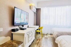 Habitación de hotel con una televisión de pantalla plana montada en la pared, un tocador blanco, una silla amarilla y dos camas.