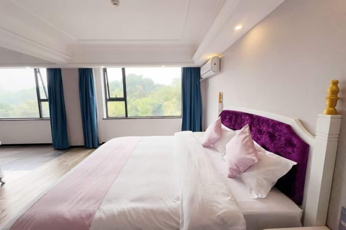 A bedroom with a large bed, a window with curtains, and a view of greenery outside.