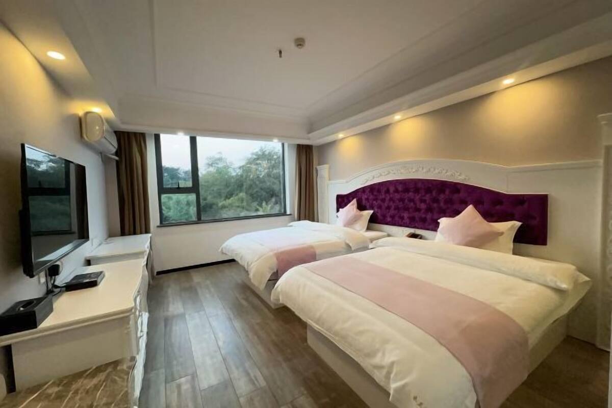 A hotel room with two beds, a TV, a desk, and a window with a view.