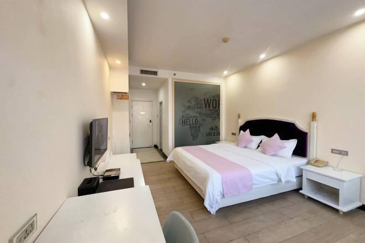 A hotel room with a bed, bedside table, TV, and a desk.