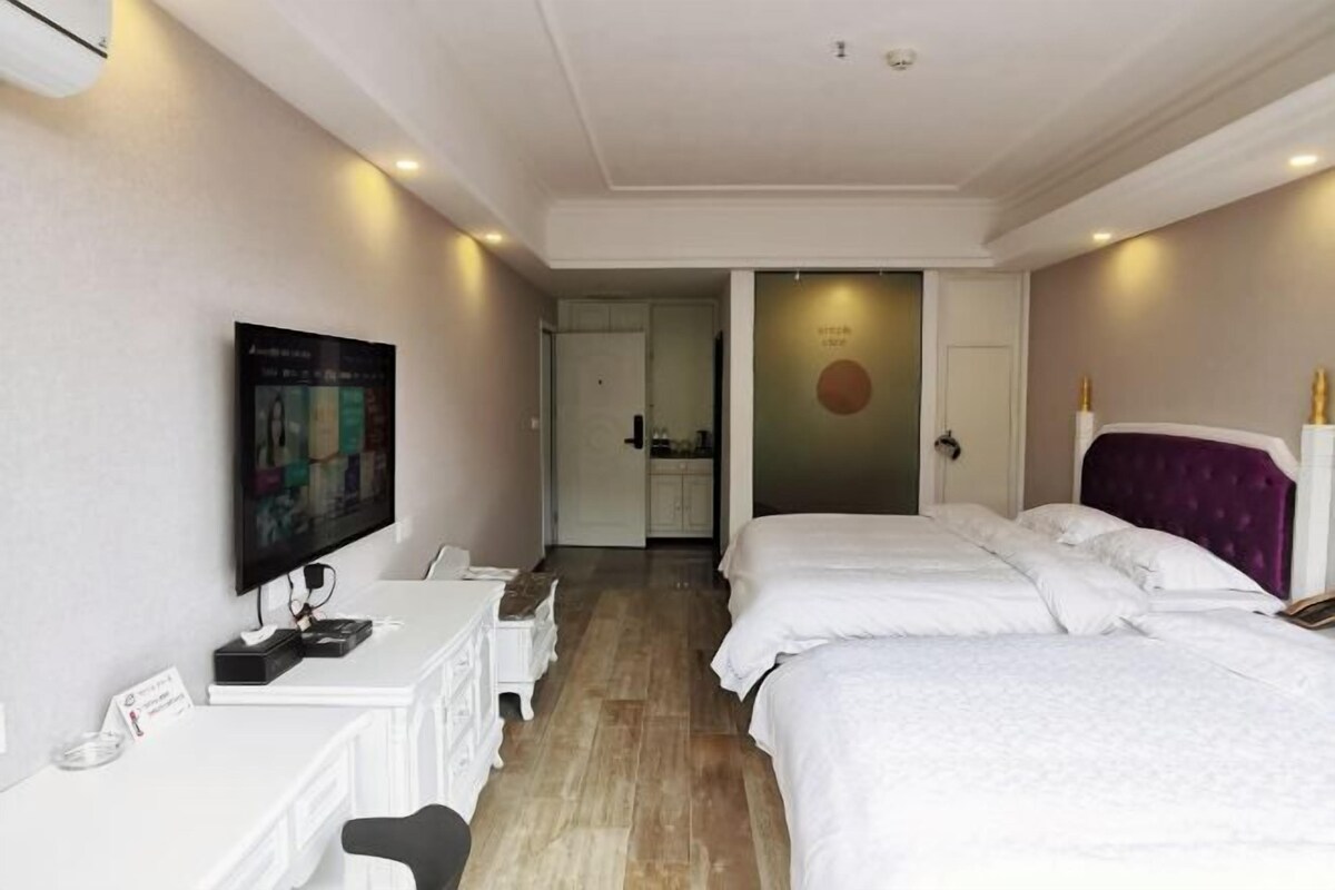 A hotel room with two beds, a desk, a TV, and a bathroom visible through an open door.